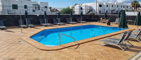 Une piscine rectangulaire, bordée d’une terrasse carrelée, entourée de chaises longues et de parasols.