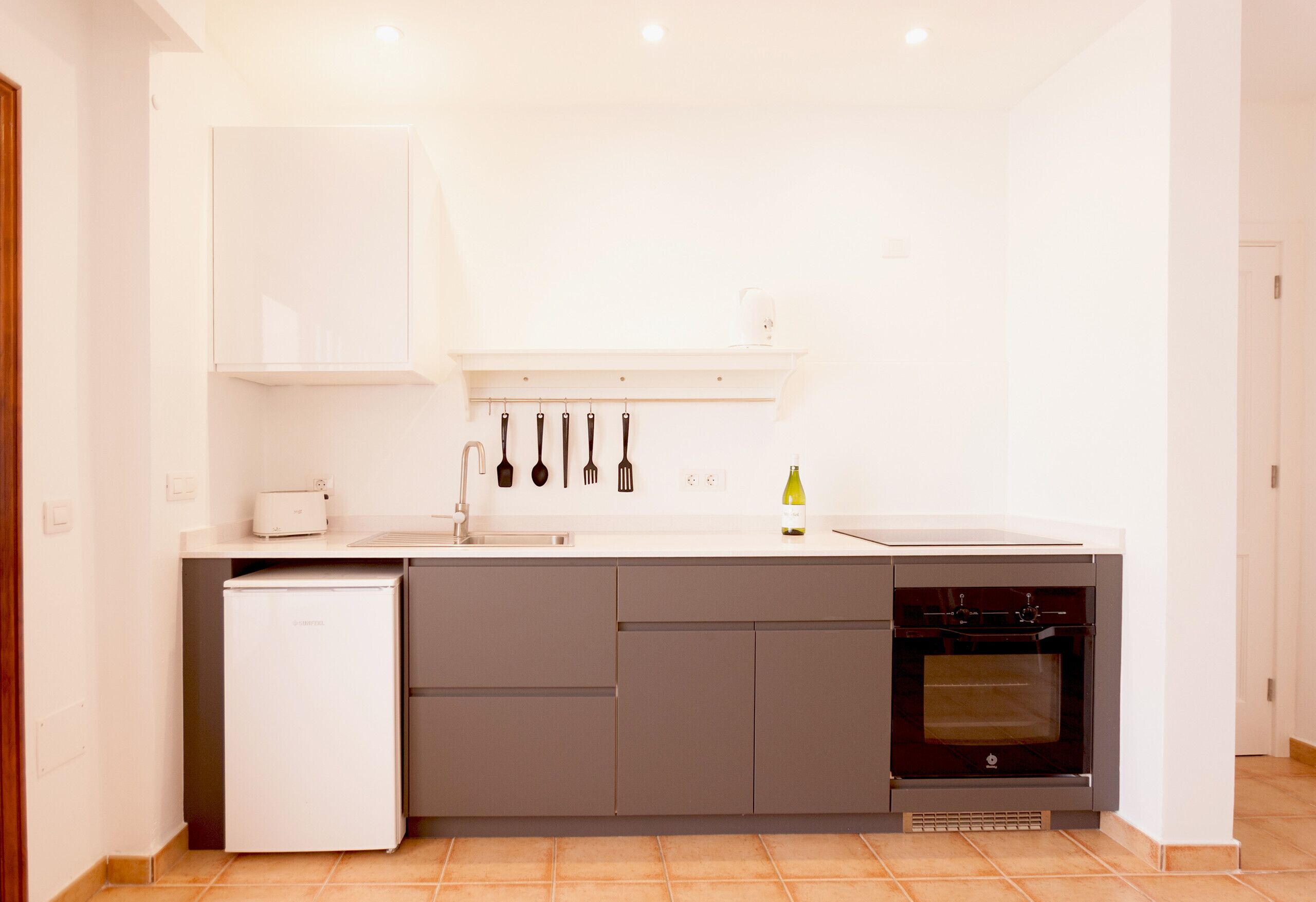 Una cocina compacta con horno empotrado, refrigerador y lavamanos.