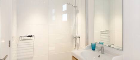 Een moderne badkamer met een douchecabine van glas, een witte wastafel met spiegel en houten opbergmeubels.