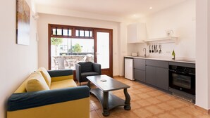 A compact living space with a sofa, a small table, a kitchenette, and a view through a glass door. - Princesa Ico 1 bedroom apts. (Puerto del Carmen)