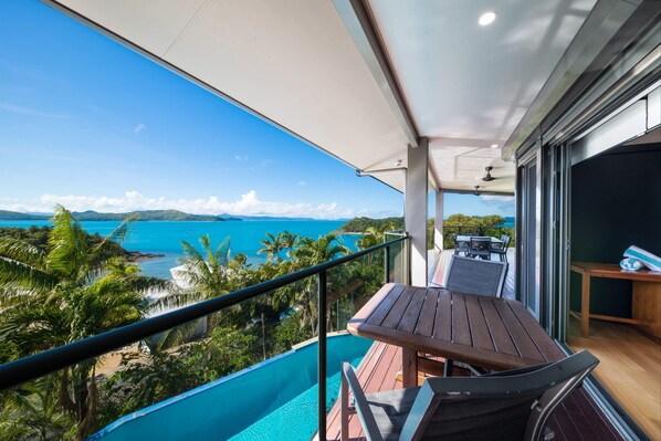 A balcony with a view of the ocean, a wooden table, and a chair.