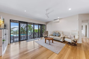 A spacious living room with a large sliding glass door leading to a balcony with a pool view, a ceiling fan, and a white sofa.