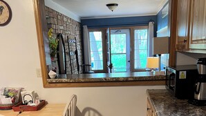 A kitchen with a wooden dining table, chairs, a large mirror, and a view of the outside through a window.