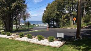 A parking lot with a view of the sea, surrounded by trees and a grassy area with a white signboard.