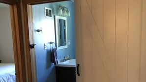 A room with a bed, a bathroom with a sink and mirror, and a sliding door.