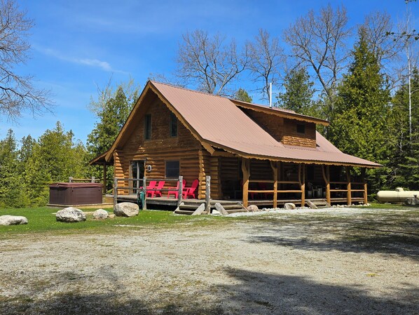 A log cabin with a porch, red chairs, and a small shed.