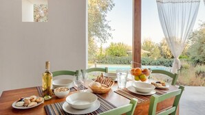 Ein Esstisch, gedeckt mit Tellern, Schüsseln, Gläsern und einer Flasche, mit Blick auf Pool und Garten.