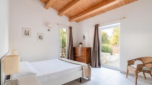 Ein Schlafzimmer mit Bett, Kommode, Stuhl und einem Vorhangfenster.