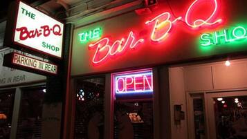 Un escaparate con letreros de neón que dicen "The Bar-B-Q Shop" y "ABIERTO".