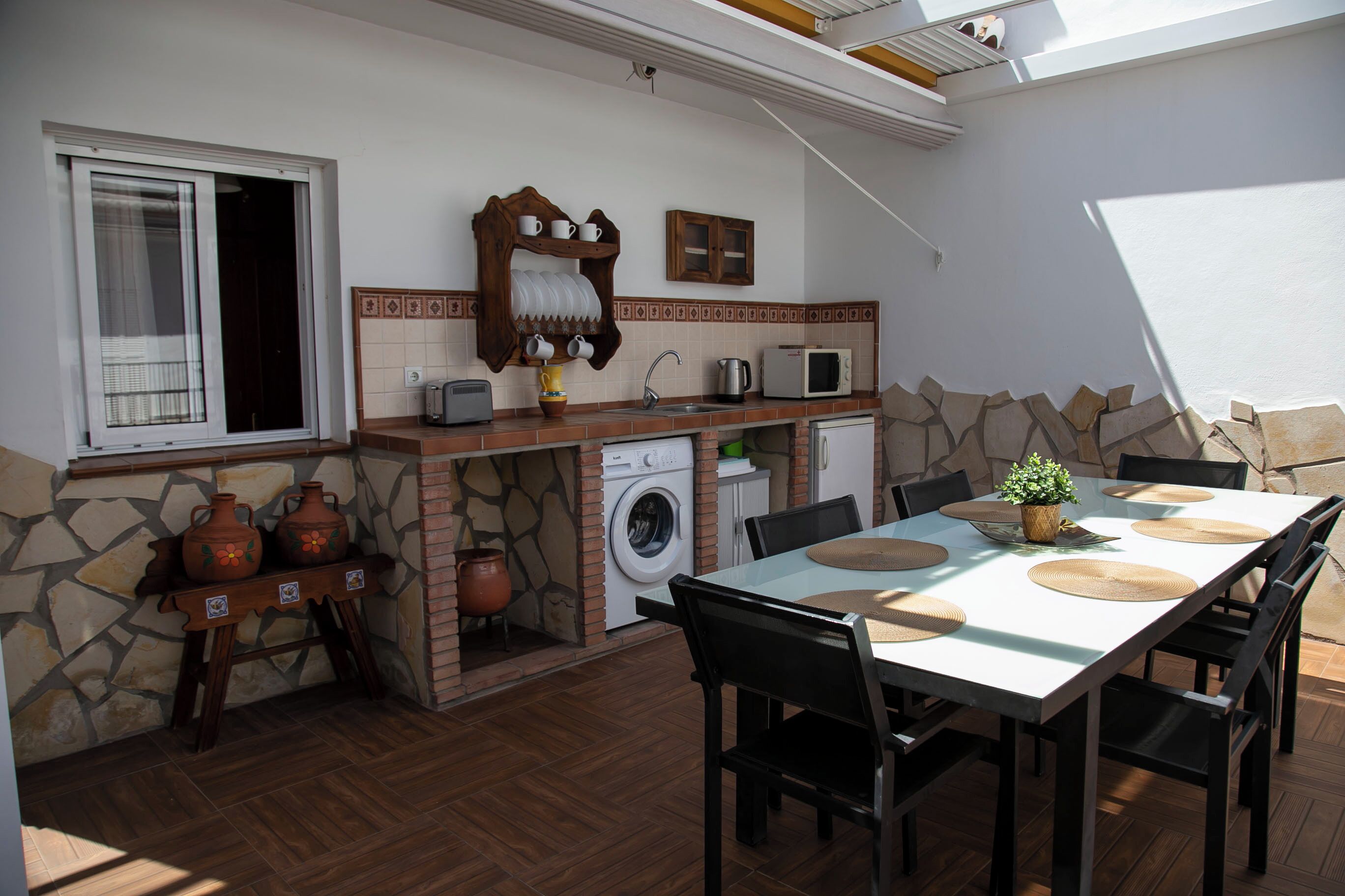 Una cocina funcional con pared de piedra, lavadora y zona de comedor con mesa y sillas.