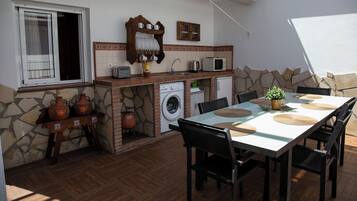 Una cocina funcional con pared de piedra, lavadora y zona de comedor con mesa y sillas.