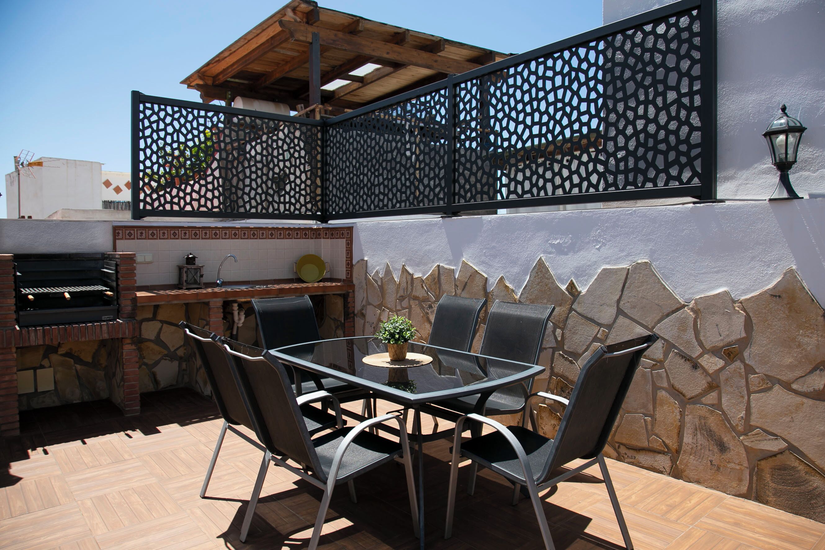 Un patio exterior con una parrilla, una mesa de comedor, sillas y un separador decorativo.
