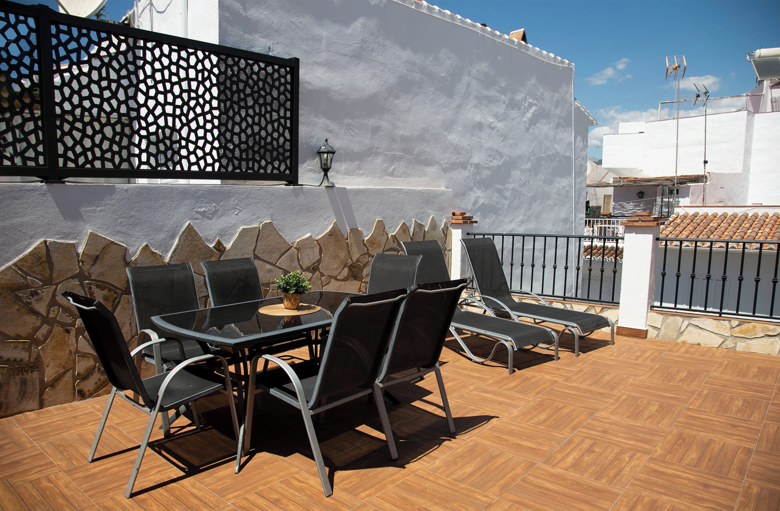 An outdoor patio with a stone wall, a black metal fence, and a tiled floor.