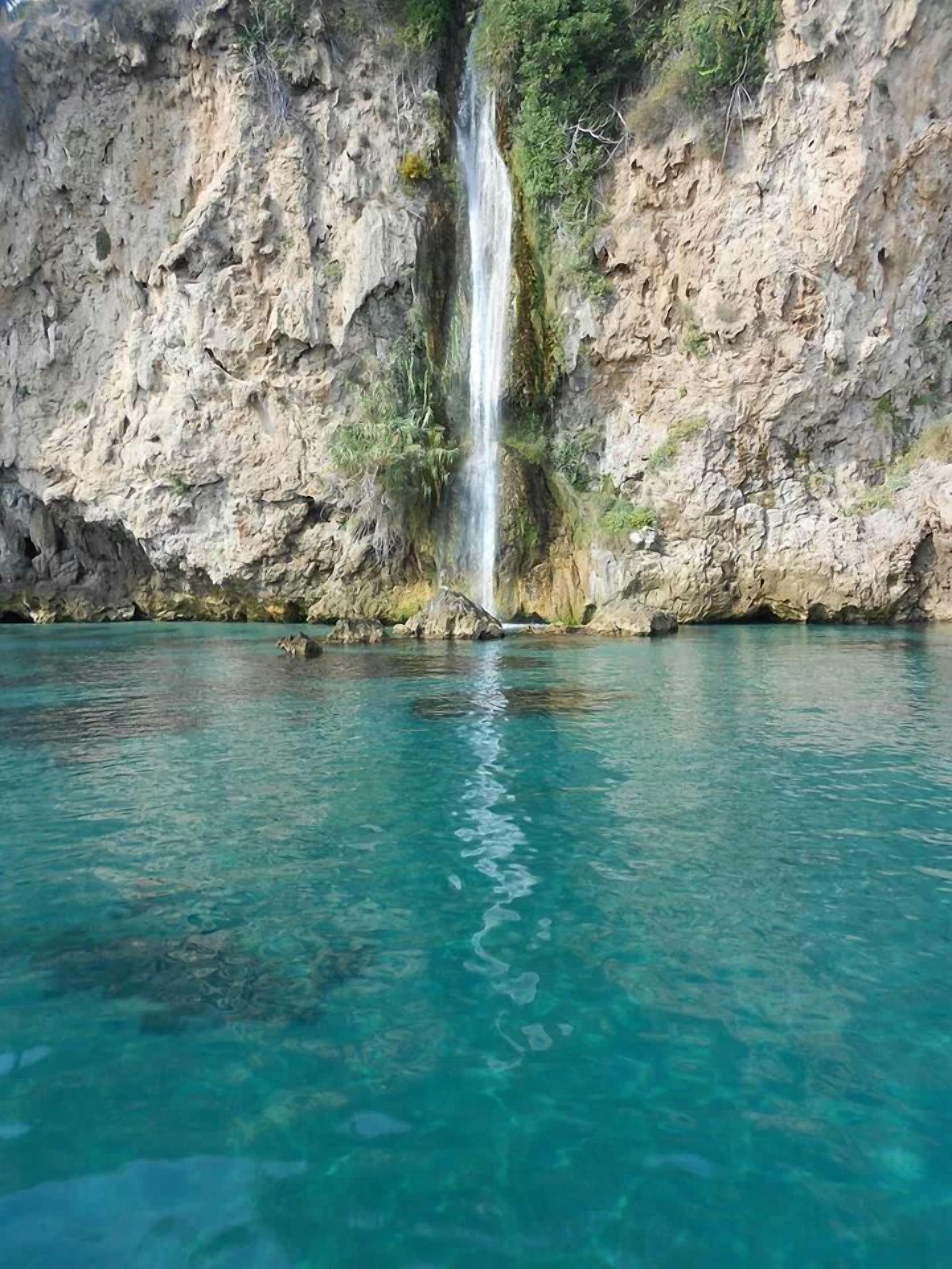 Una cascada cristalina se precipita en una piscina turquesa, rodeada de acantilados rocosos.