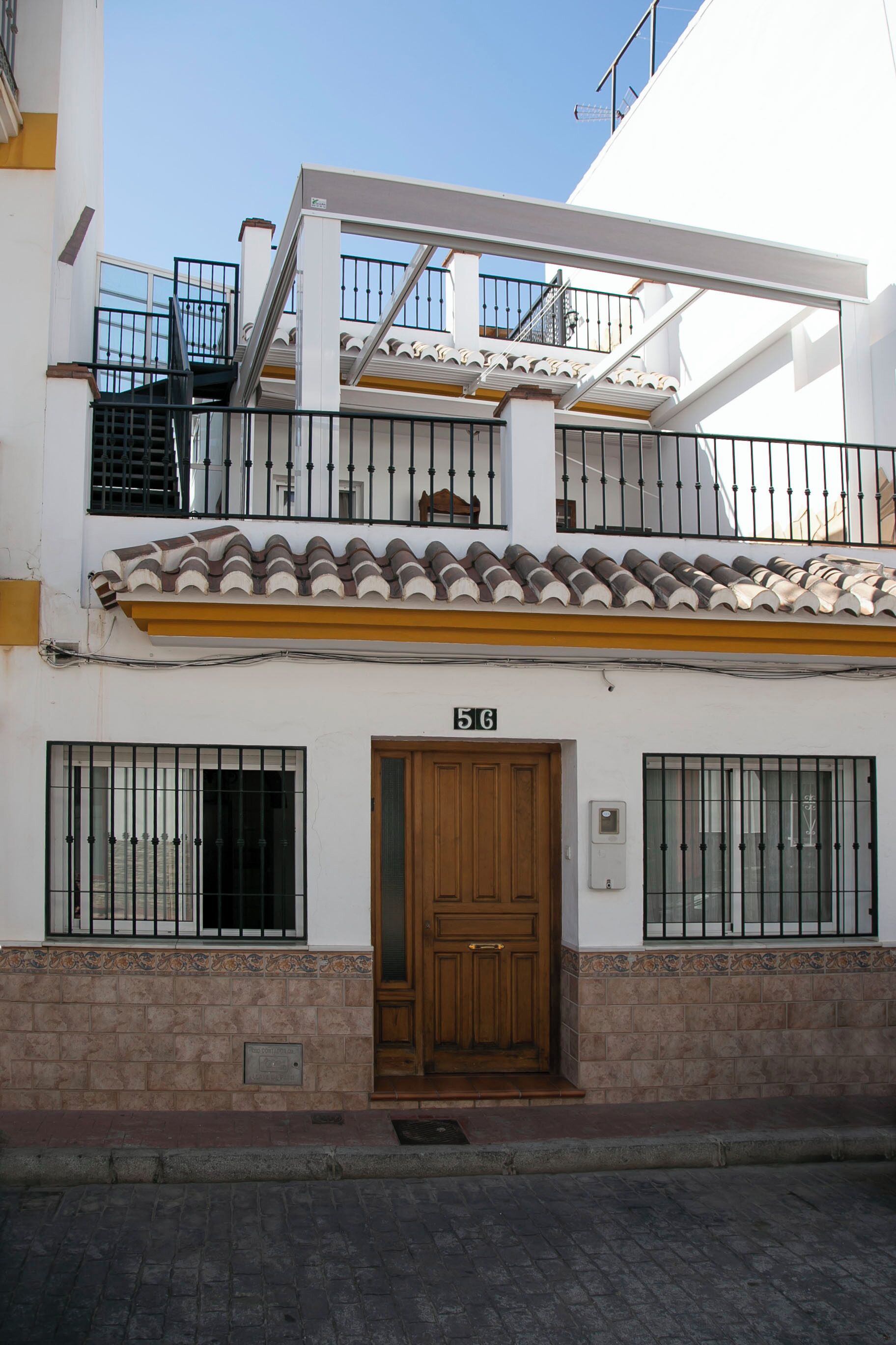 A two-story building with a wooden door, numbered 56, and a balcony with metal railings.