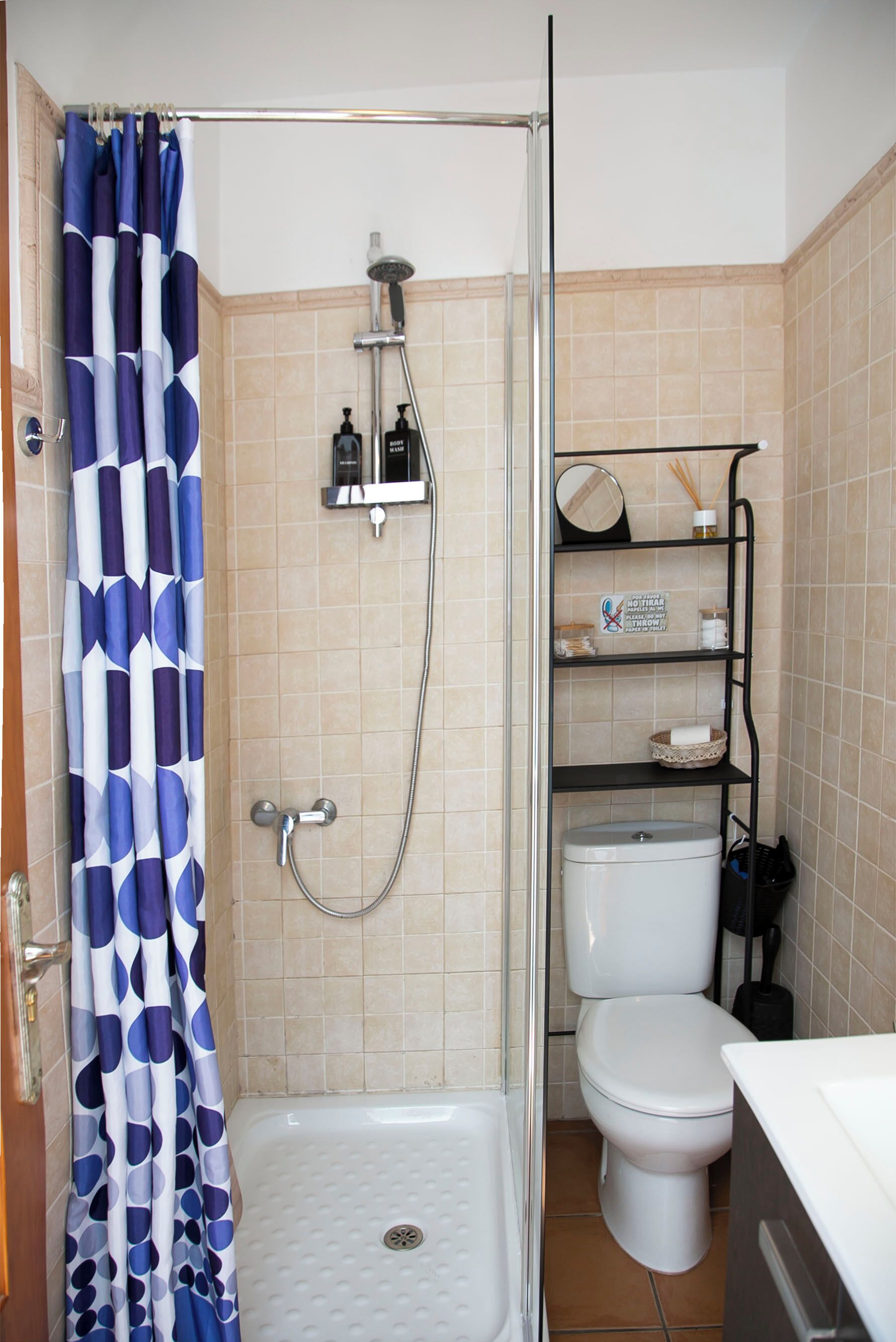 Un baño con ducha, inodoro y estante con artículos de aseo.