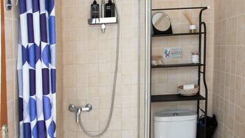 Un baño con ducha, inodoro y estante con artículos de aseo.