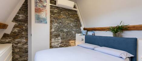 Un dormitorio con pared de piedra, cama con ropa de cama a rayas, mesita de noche y una planta en maceta.