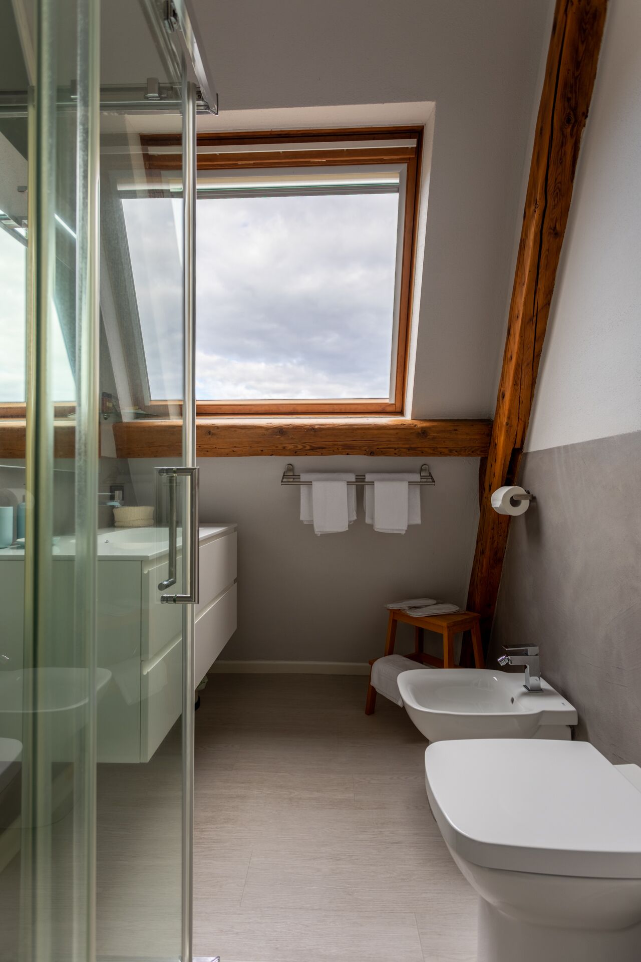Une salle de bain moderne avec un puits de lumière, deux lavabos, une douche en verre et des poutres en bois.