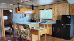 A compact kitchen with wooden cabinets, a black refrigerator, and a bar stool. - Northern Maine Lake Camp (Millinocket)