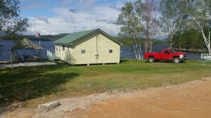 A small, single-story building with a green roof, situated by a lake. - Northern Maine Lake Camp (Millinocket)