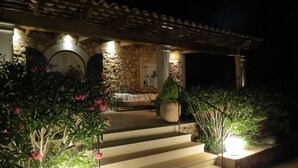 Ein Steinhaus mit überdachter Außenbestuhlung, Stufen, die hinauf führen, und umgebenden Pflanzkübeln.