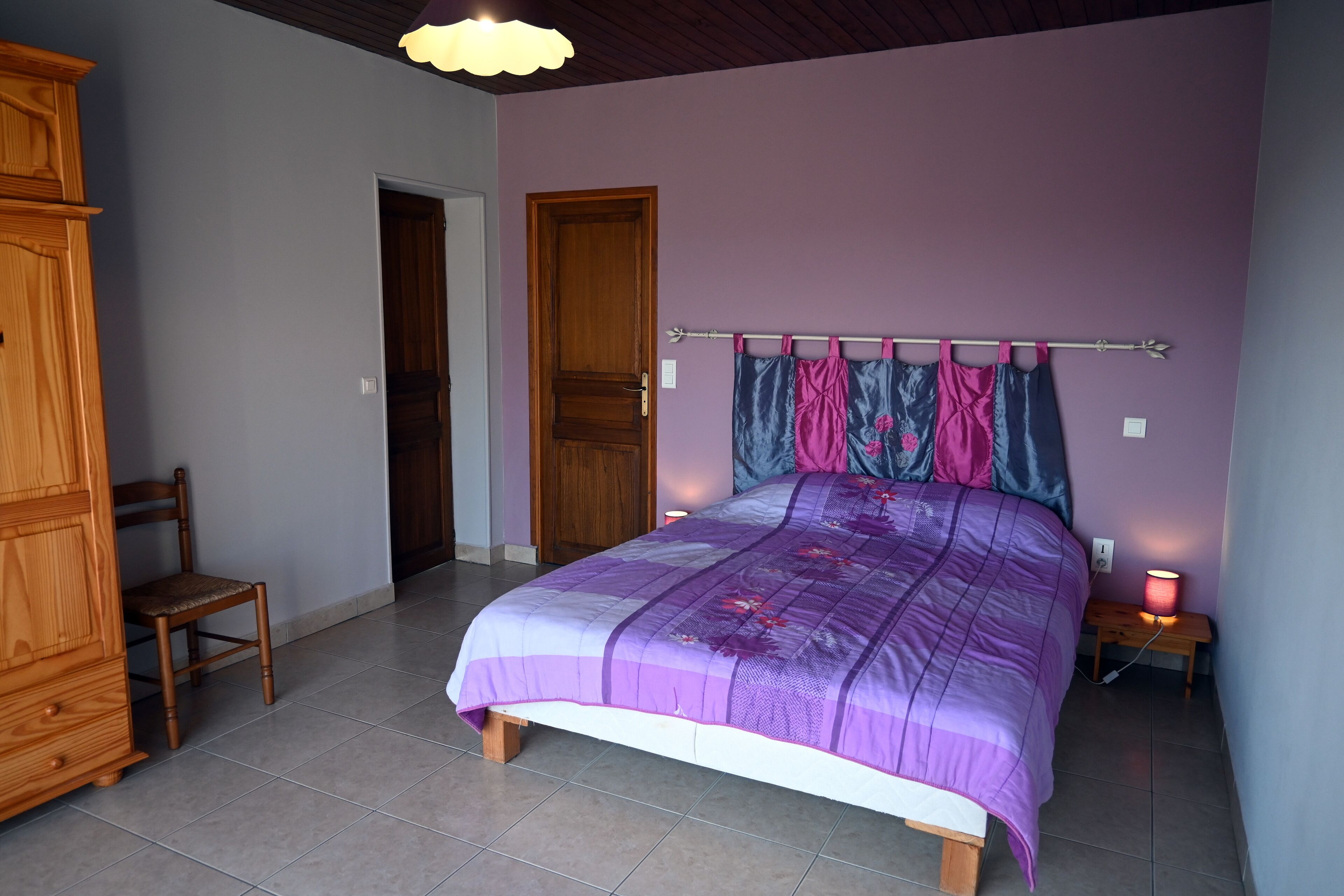 A bedroom with a bed, wooden furniture, and a nightstand with a lamp.