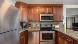 A modern kitchen with stainless steel appliances, wooden cabinets, granite countertops, and a built-in oven.