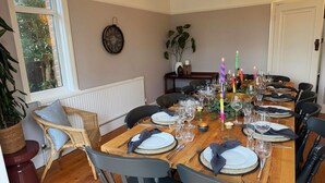 Un comedor con una mesa de madera dispuesta para una comida, rodeada de sillas, con una planta y un reloj en la pared.