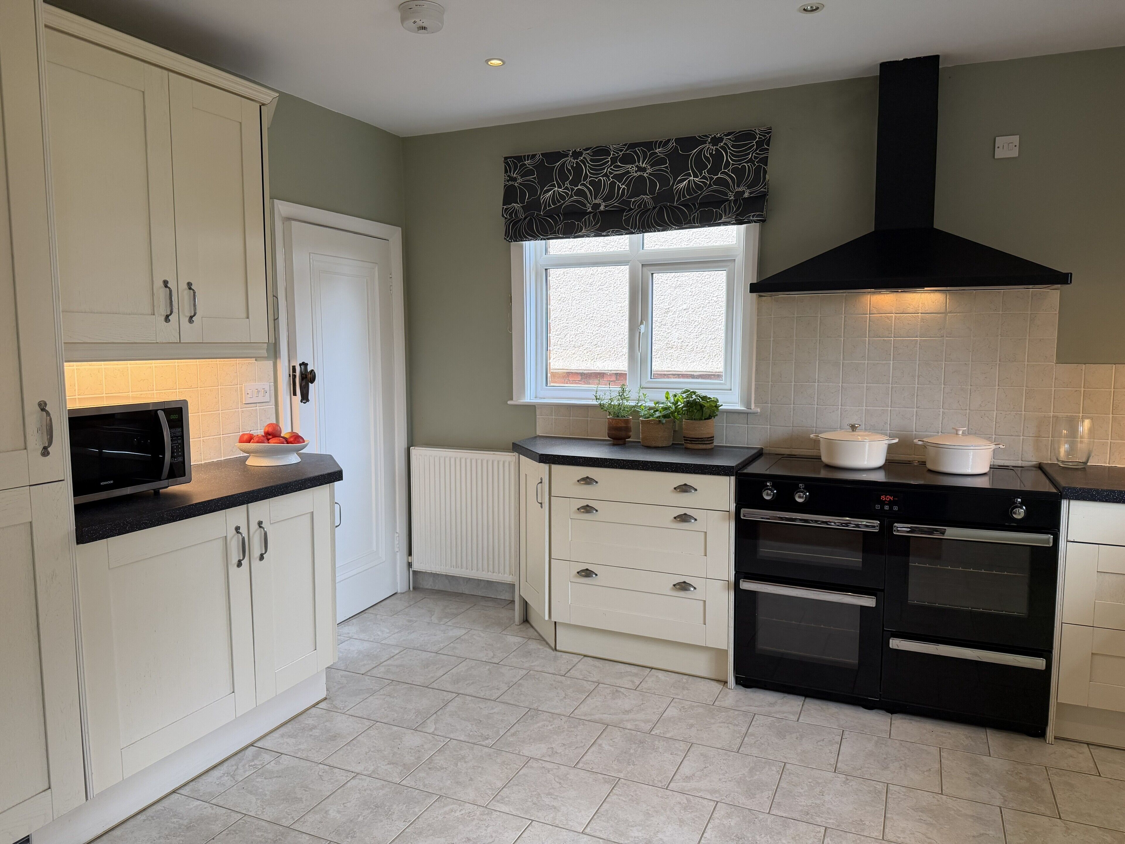 A kitchen with white cabinets, a black microwave, a stove, and a window with a black valance.