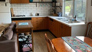 A compact kitchen with a dining area, wooden cabinets, a microwave, a stove, and a window with a view. - Pyrenees Farm Stay Amphitheatre. (Pet friendly) Bed and Breakfast. (Amphitheatre)
