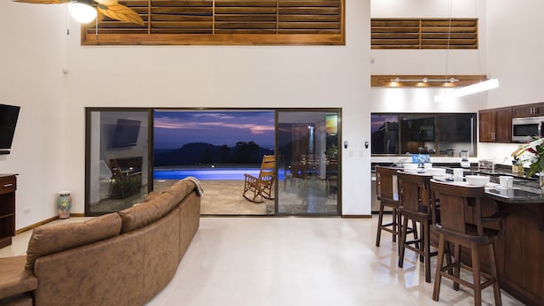 Una cocina moderna con taburetes de bar, una isla grande y vistas a una piscina al anochecer.