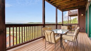 Terraza de madera con una mesa y sillas de vidrio, con vista a un paisaje.