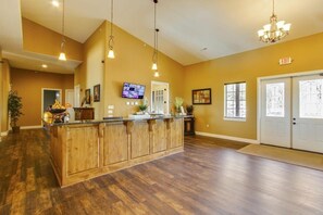 A spacious lobby with a wooden reception desk, a mounted TV, and a chandelier.