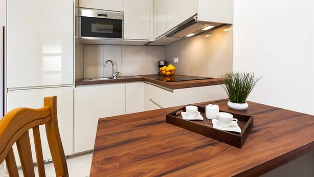 Een moderne keuken met witte kasten, een roestvrijstalen oven, een ingebouwde magnetron en een houten aanrecht met een schaal witte kopjes en een potplant.