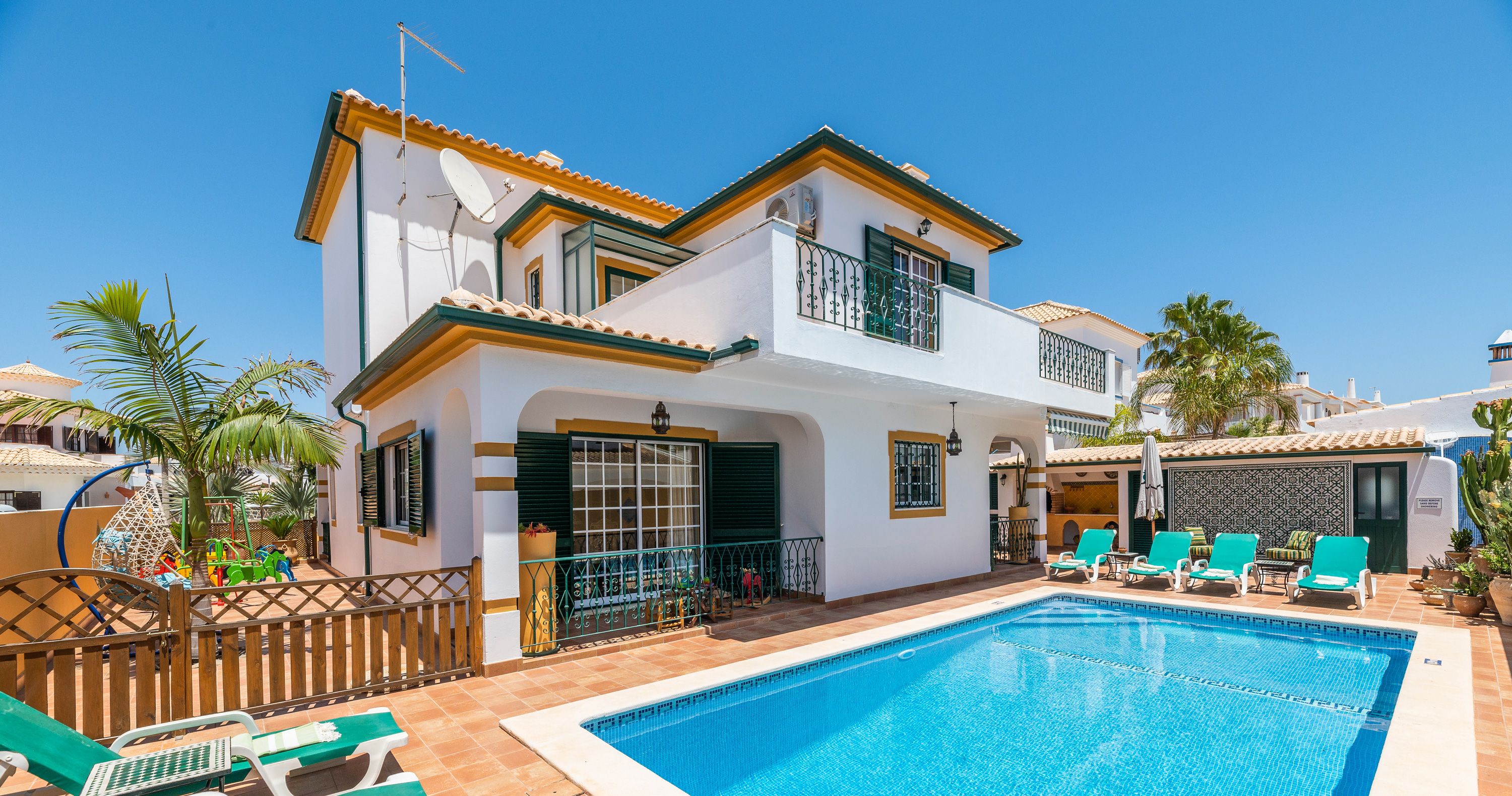 A two-story house with a swimming pool, green lounge chairs, and a fenced patio area.