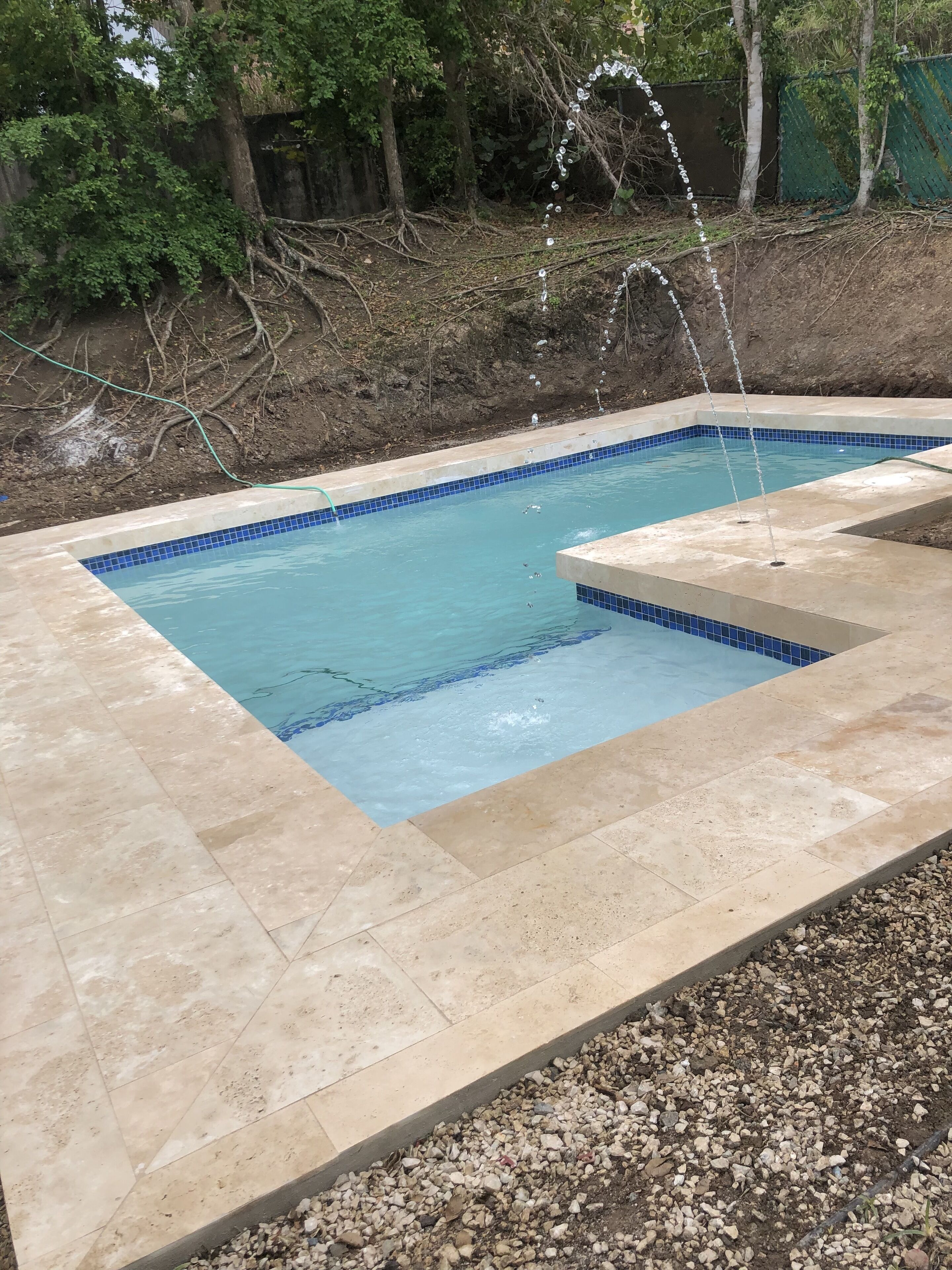 A rectangular swimming pool with a blue tiled edge, surrounded by beige tiles and a pebble border.