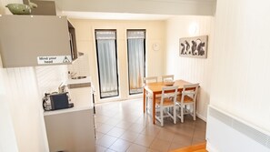 A kitchen with a sink, a coffee machine, and a cabinet. There is a dining area with a table and chairs.