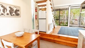 A compact kitchen with a dining area, a refrigerator, and a window overlooking a garden. - ALLAMBIE COTTAGES - VILLA 3: Bright (Bright)