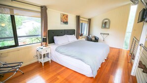 A bedroom with a large bed, a nightstand with a lamp, a chair, and a window with curtains. - ALLAMBIE COTTAGES - VILLA 3: Bright (Bright)