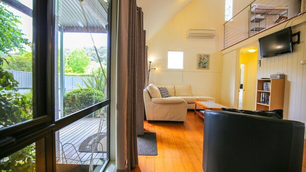 A cozy living room with a sofa, a coffee table, and a TV. There's a balcony with a view of greenery. - ALLAMBIE COTTAGES - VILLA 3: Bright (Bright)