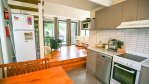 A compact kitchen with a refrigerator, microwave, stove, and a dining area with a wooden table and chairs. - ALLAMBIE COTTAGES - VILLA 3: Bright (Bright)