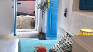 A room with a view of the sunset over the sea, a blue door, a potted plant, and a vase with a flower.