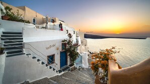 A white building with a blue door and stairs leading to a balcony overlooking the sea.