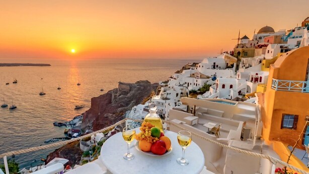 A seaside view with boats, a sunset, and a table with fruit and wine glasses.