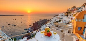 Une vue sur la mer avec des bateaux, un coucher de soleil et une table avec des fruits et des verres à vin.
