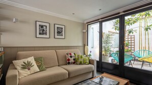 A living room with a beige sofa, a coffee table, and two framed pictures on the wall. - Stunning Studio With Private Patio In Charming Gated Street (Neuilly-Sur-Seine)
