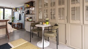 A dining area with a round table and two chairs, a bookshelf, and a radiator. - Stunning Studio With Private Patio In Charming Gated Street (Neuilly-Sur-Seine)