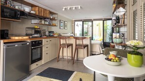 A modern kitchen with wooden cabinets, a dishwasher, and a dining area with a table and chairs. - Stunning Studio With Private Patio In Charming Gated Street (Neuilly-Sur-Seine)