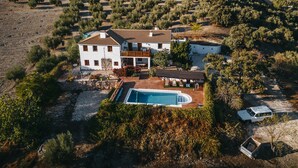 Ein zweigeschossiges Haus mit Swimmingpool, umgeben von Olivenbäumen und einer hügeligen Landschaft.